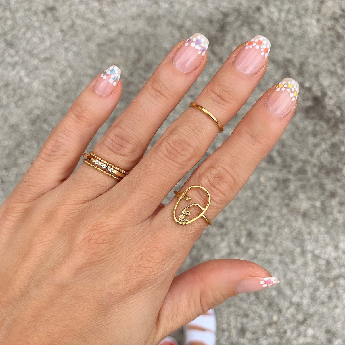 Artist Face Ring alongside other dainty gold stacking rings by Katie Dean Jewelry as seen on a manicured hand with flower details.