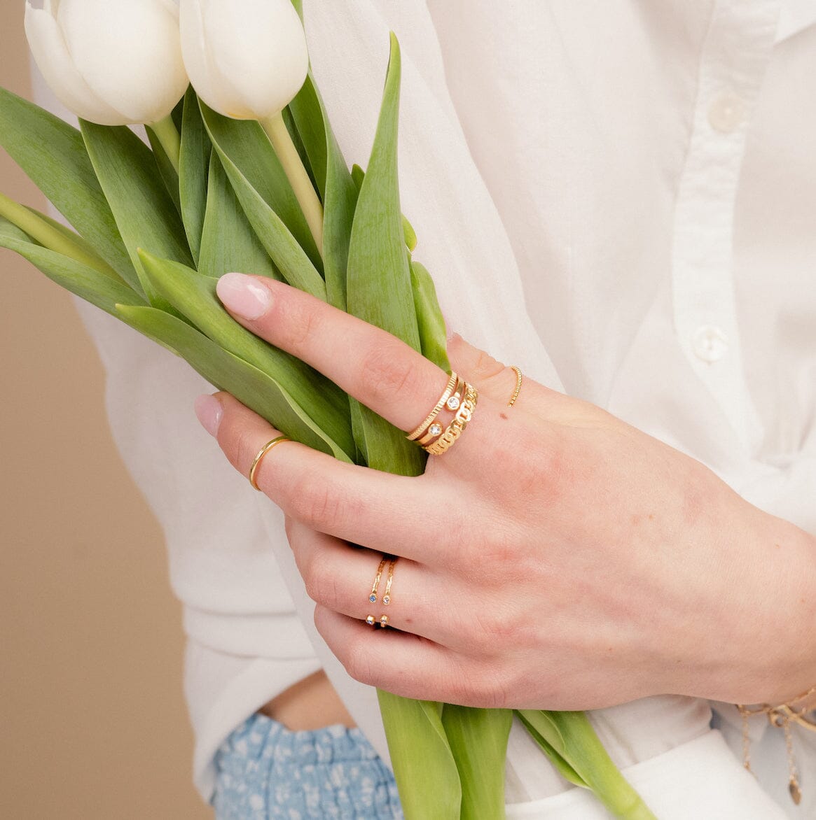 Image showing dainty gold rings on the hand of a model holding white tulips, made in America by Katie Dean Jewelry.