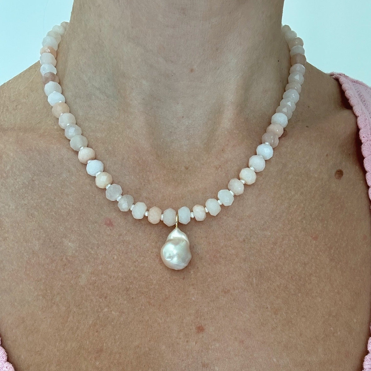 Pearl necklace with a baroque pearl pendant worn by a person in a pink top against a light background.
