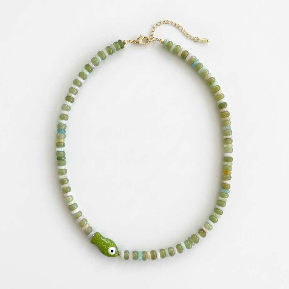 Necklace with green beads and green fish-shaped pendant on a white background
