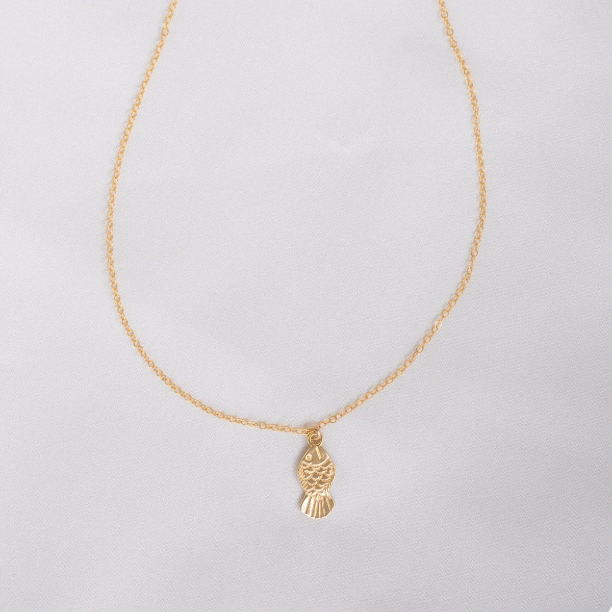 Gold necklace with a fish pendant on a light gray background