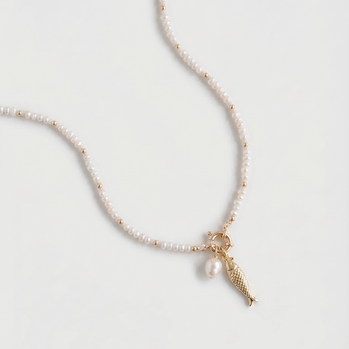 Pearl necklace with a gold fish charm on a light gray background