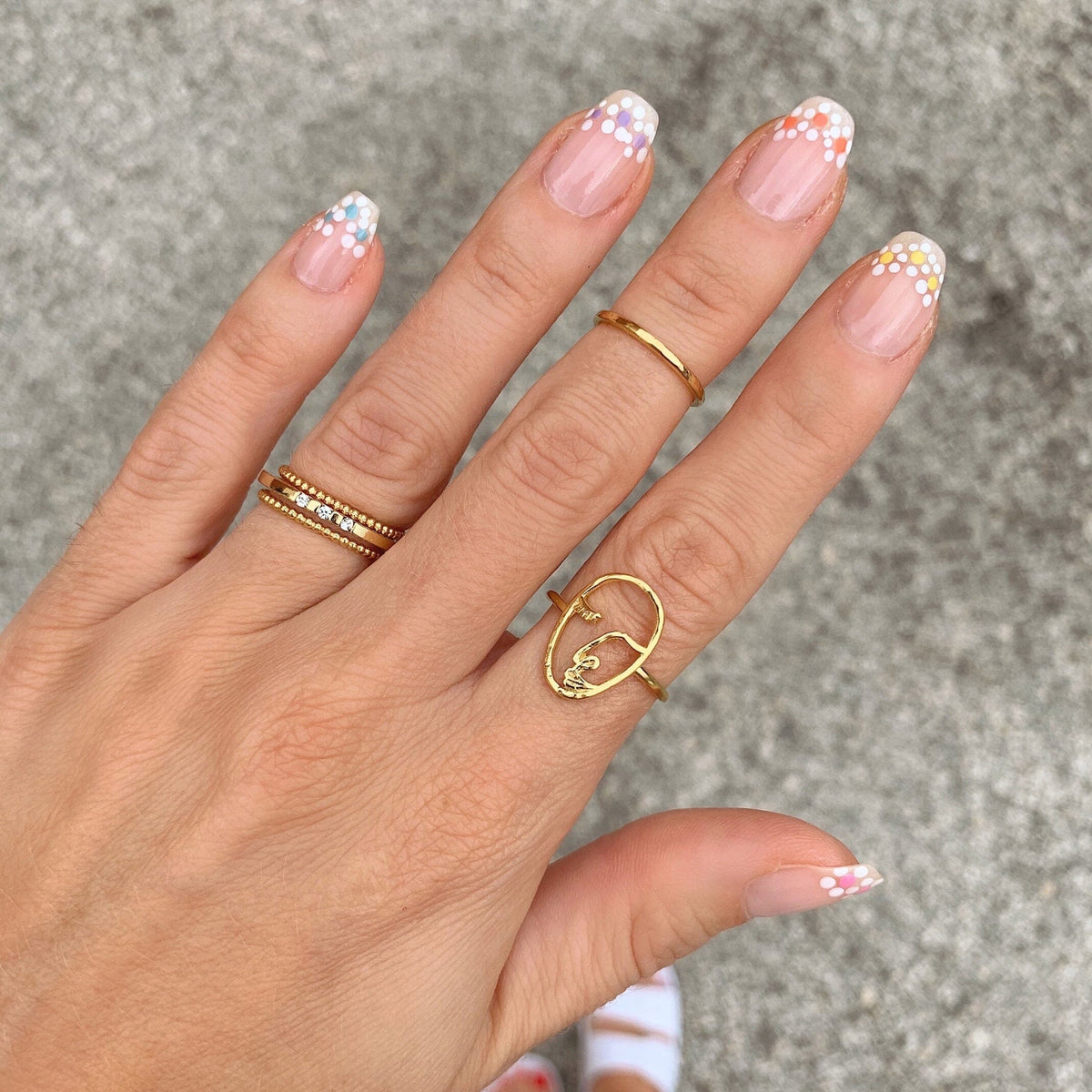 Artistic hand pose showcasing Katie Dean Jewelry rings including the Artist Face Ring with floral nail design.