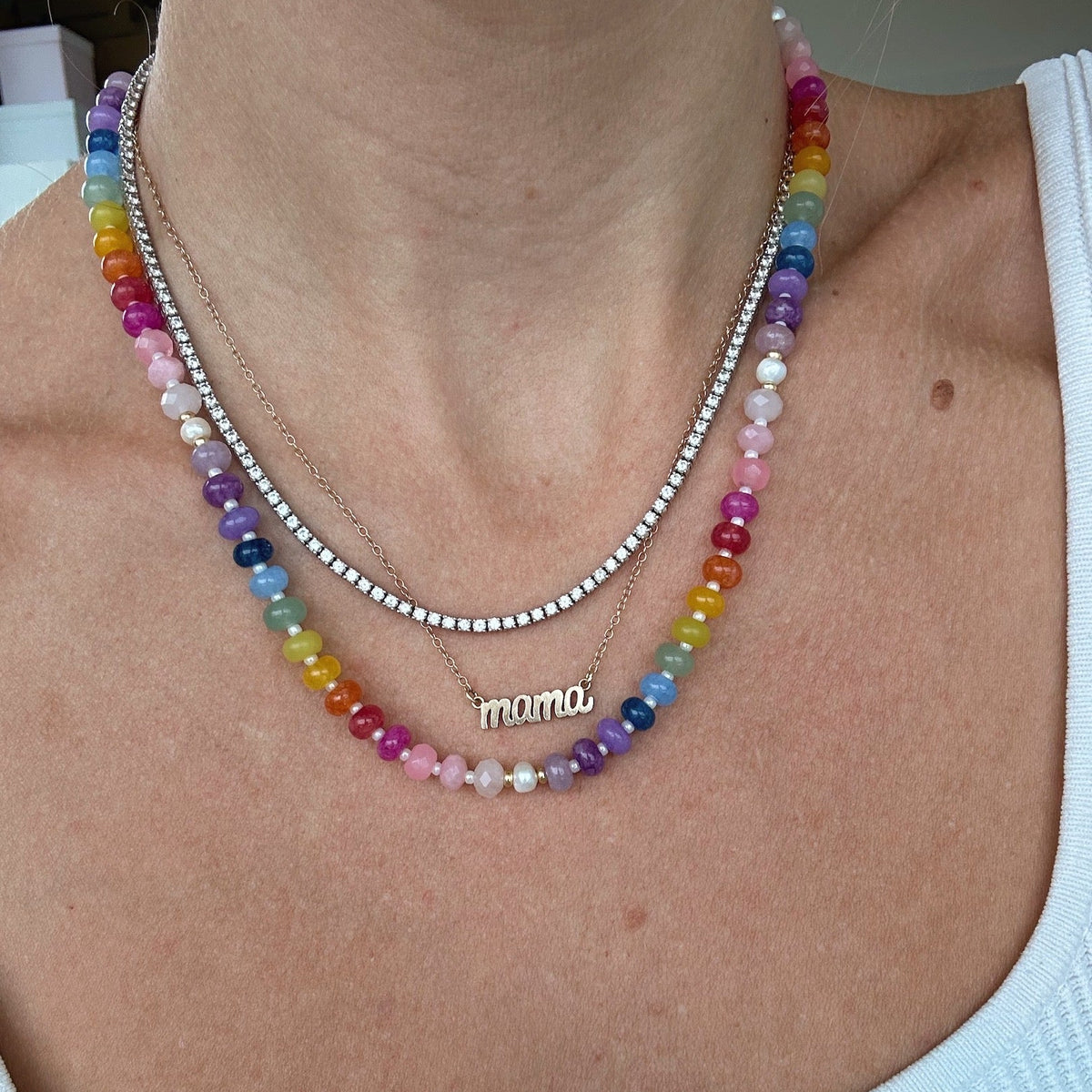 Colorful beaded rainbow necklace with gold and pearl accents, layered with the 'mama' necklace and diamond necklace on a person wearing a white tank top. Made By katie Dean Jewelry.