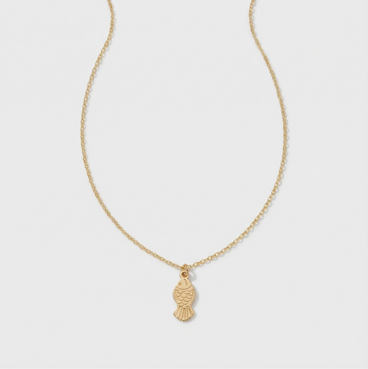 Gold necklace with a fish pendant on a light gray background