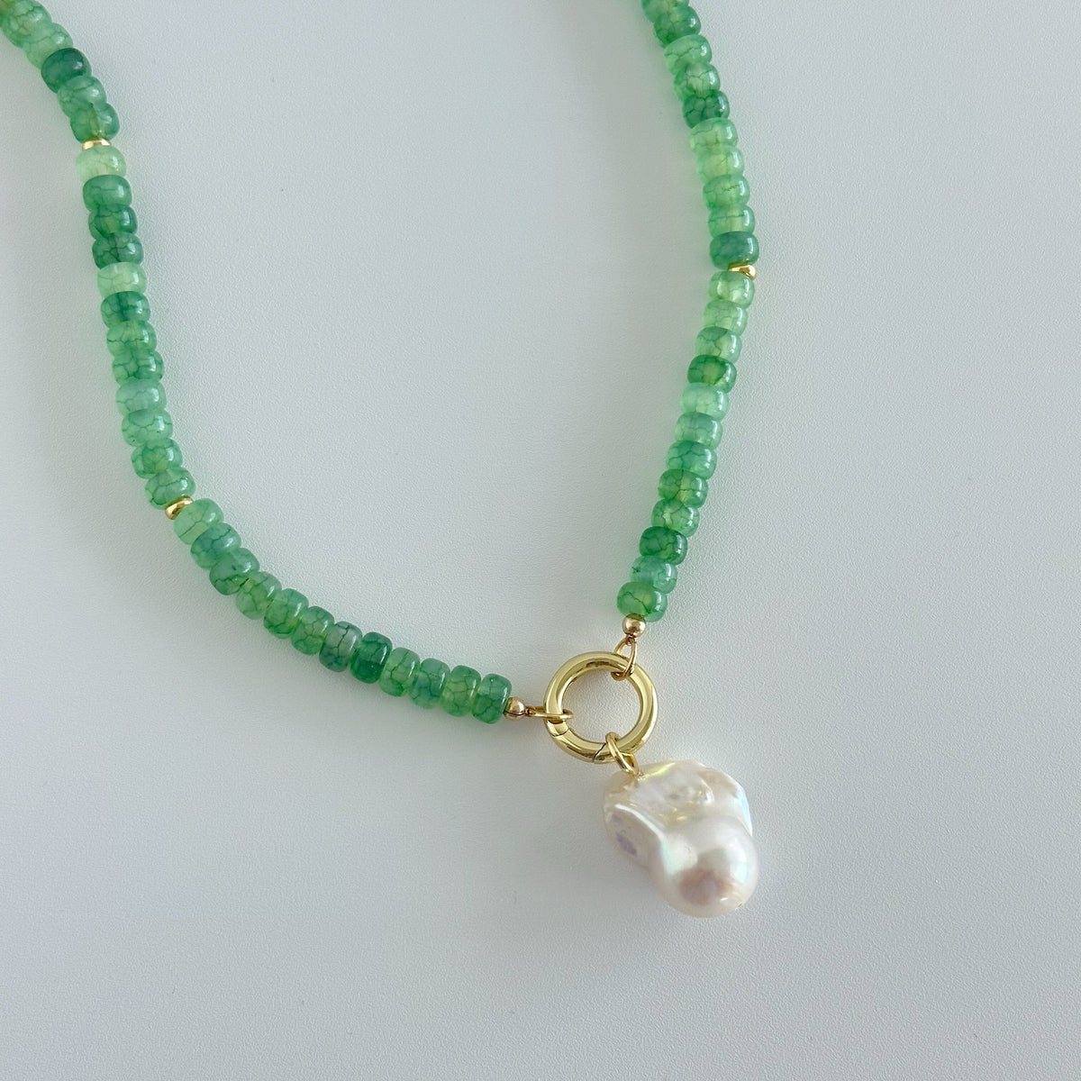 Green beaded necklace with a gold clasp and pearl charm on a light gray background