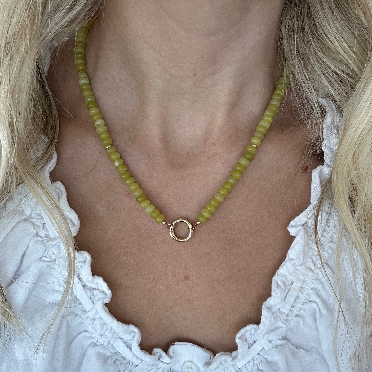 Green gemstone beaded necklace with gold fill carabiner clasp worn by a woman in a white top.