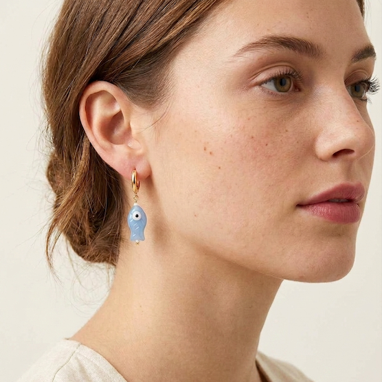 Close-up of a woman wearing a blue fish earring on a plain background