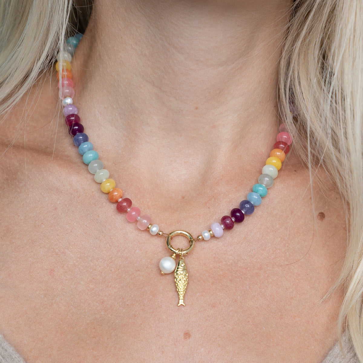 Necklace with colorful beads and a gold fish charm on a person's neck.