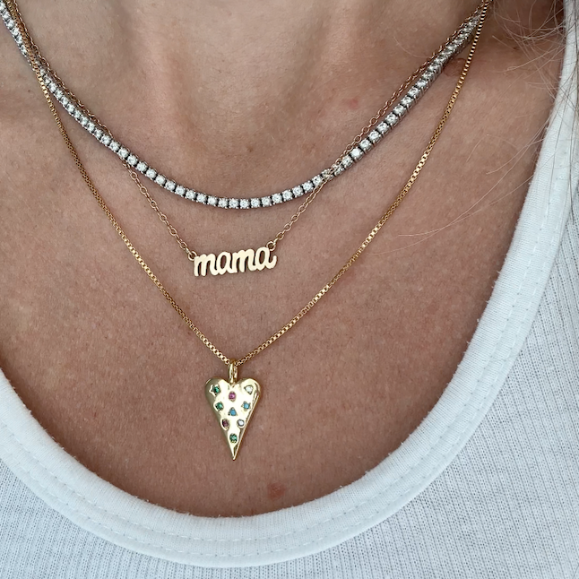 Necklace with 'mama' pendant and dainty gold heart pendant necklace with multicolor gemstone accents on a delicate chain on a person wearing a white tank top. 
