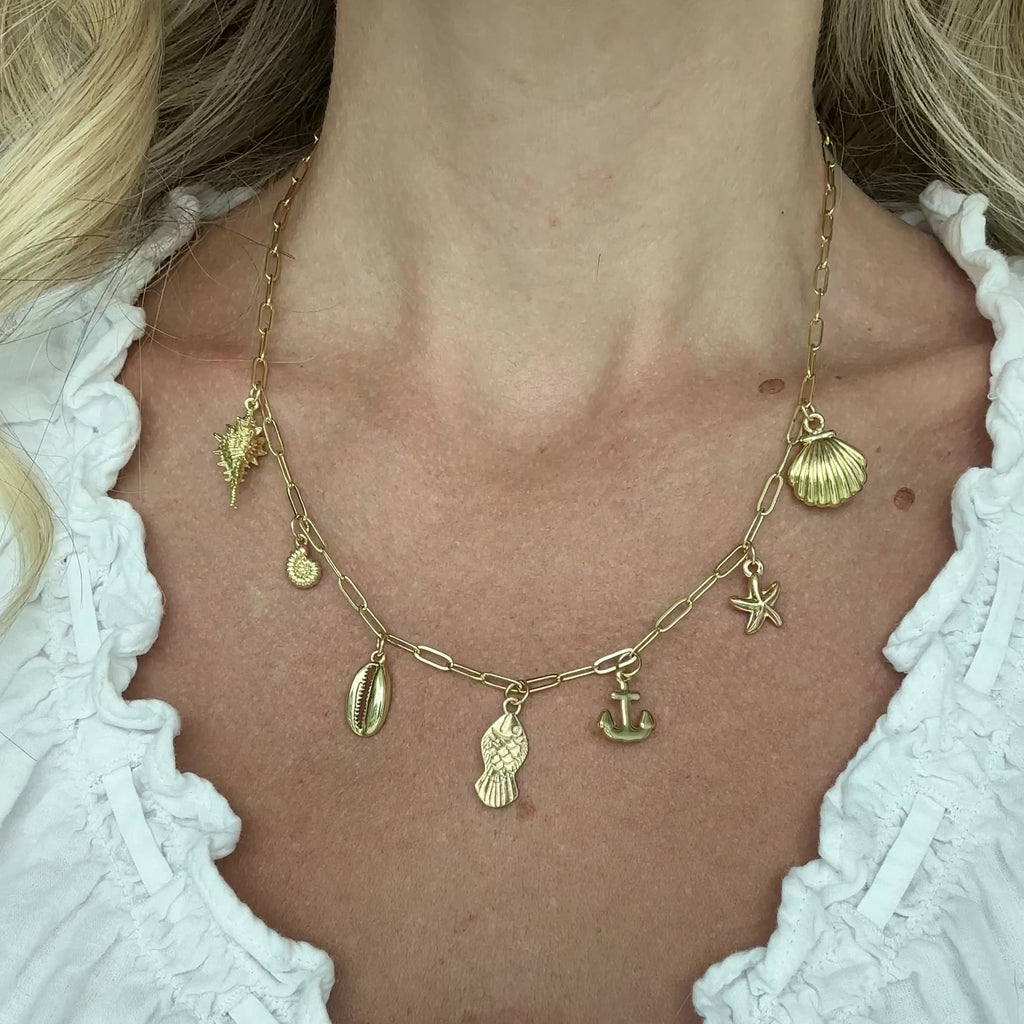 Gold necklace with various charms worn by a person in a white top.