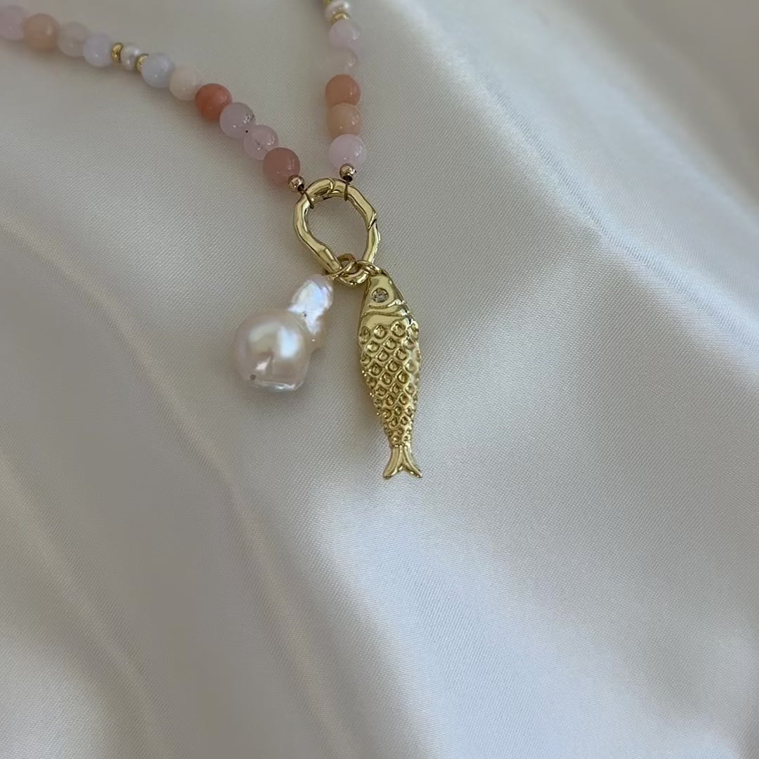 Necklace with beads and a gold fish charm and baroque pearl charm on a white background.