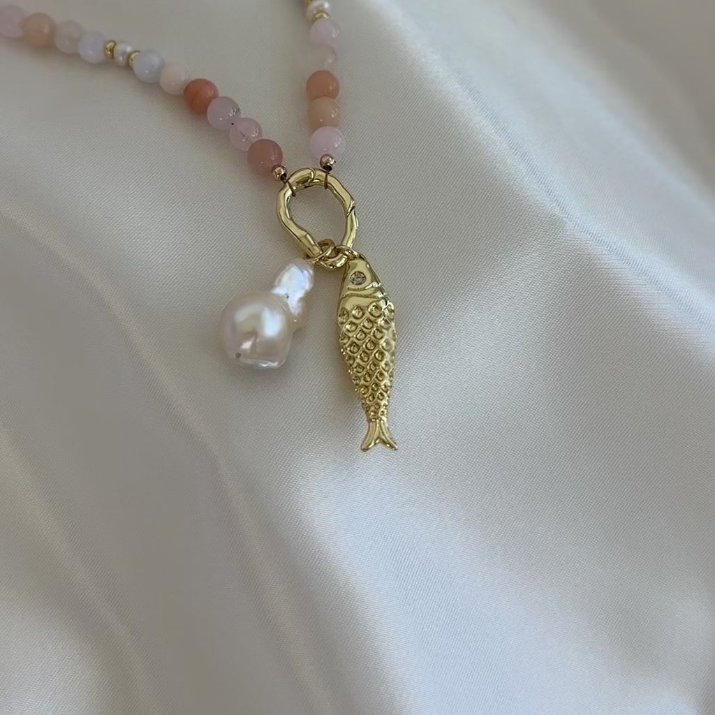 Necklace with beads and a gold fish charm and baroque pearl charm on a white background.