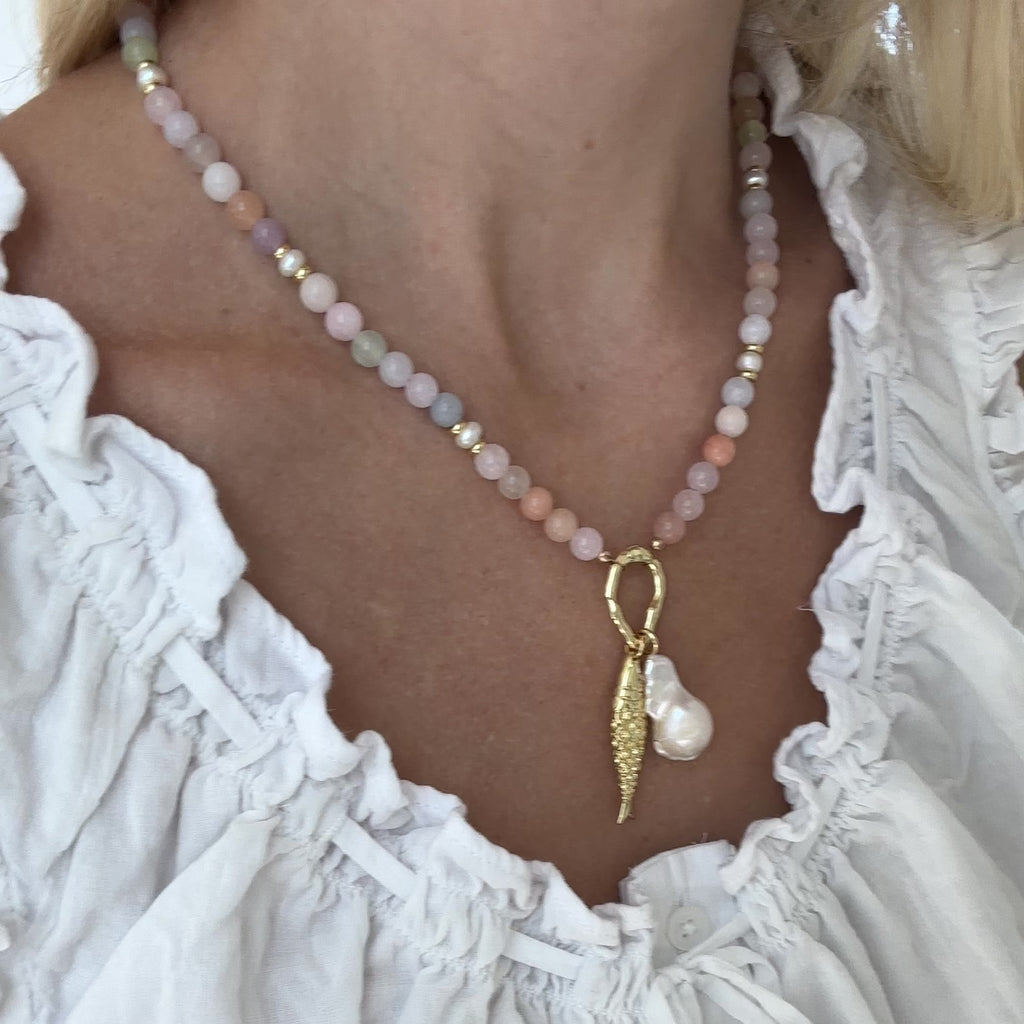Necklace with beads and a gold fish charm and baroque pearl charm on woman.