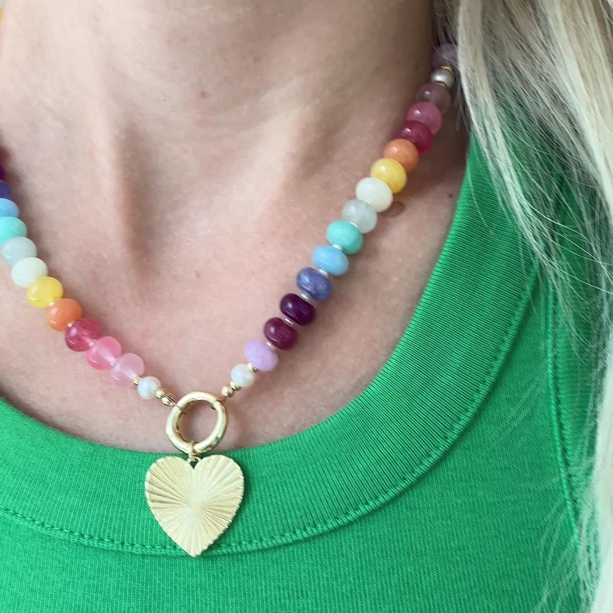 Necklace with colorful beads and a gold clasp with gold heart charm on a woman wearing a green shirt.