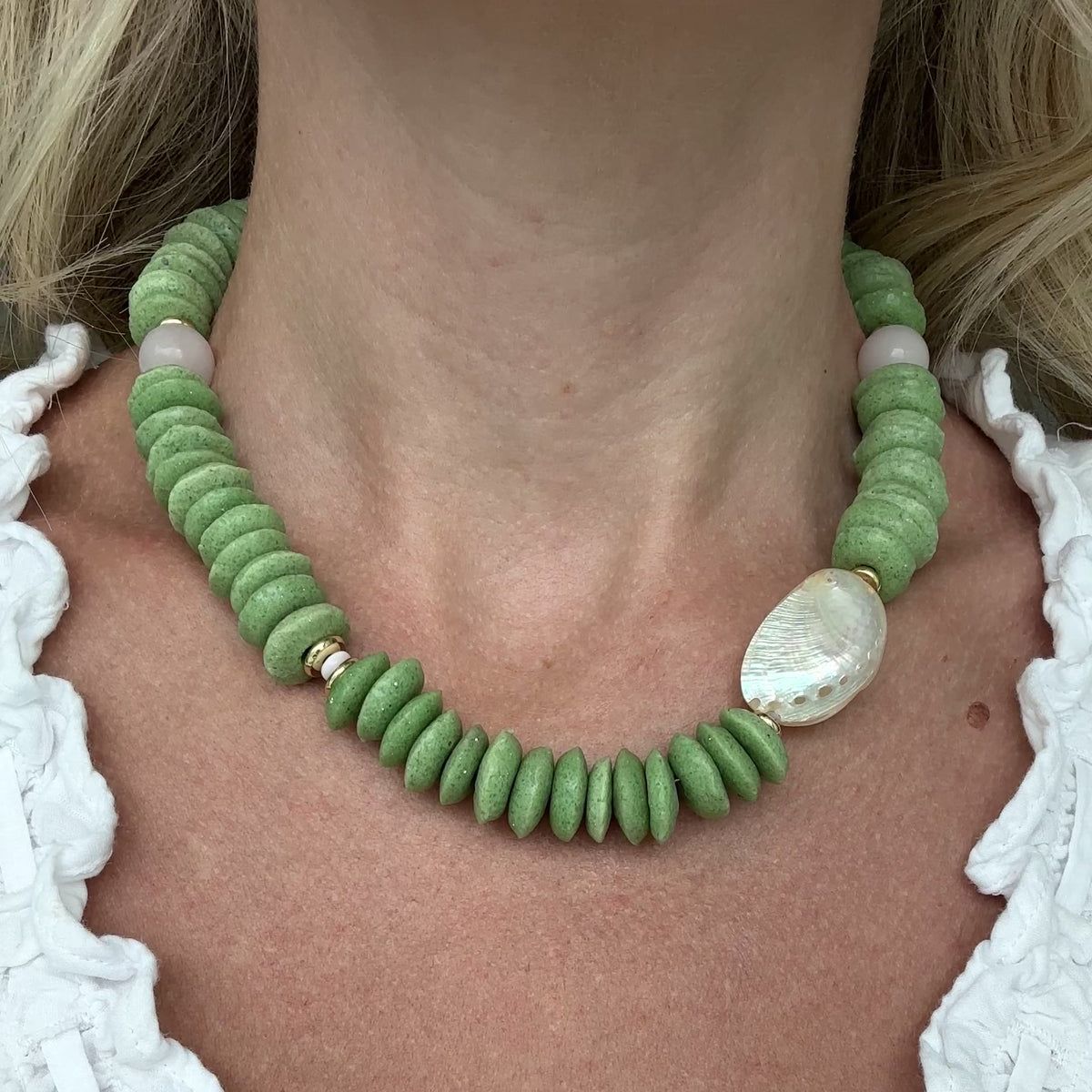 Necklace with green beads and white abalone shell and light pink quartz beads with gold elements on a person.