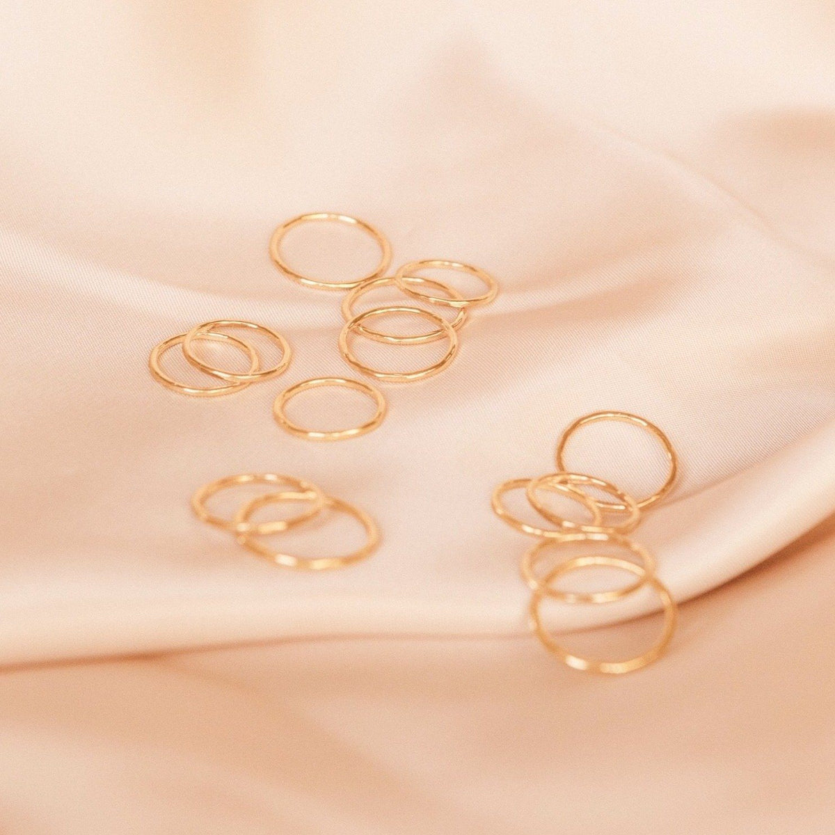 Dainty gold hammered band rings laid out on a piece of pink satin. Handmade by Katie Dean Jewelry in California.