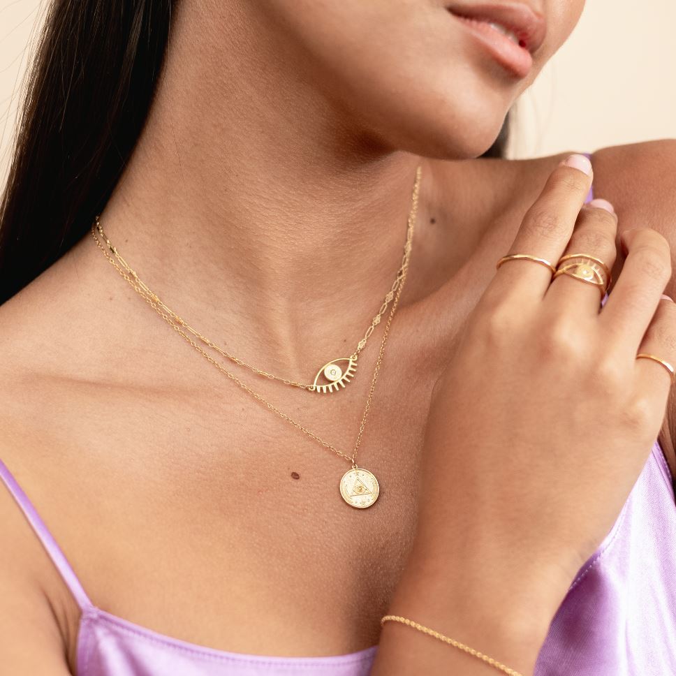 Picture of models chin and upper body wearing two gold dainty necklaces, one evil eye necklace and one all seeing eye circle pendant necklace handmade by Katie Dean Jewelry.