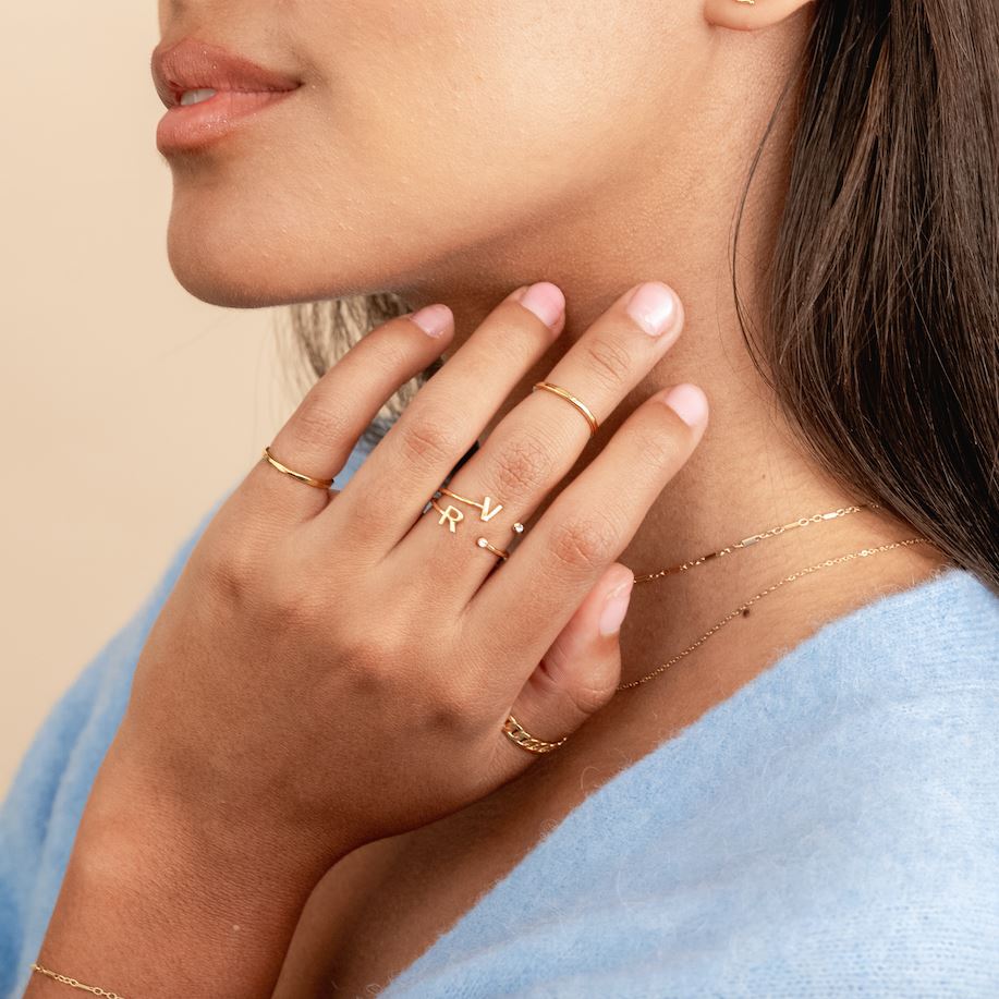 Two hands showing in the center of the image wearing the Initial Rings and Hammered Band Rings made by Katie Dean Jewelry.
