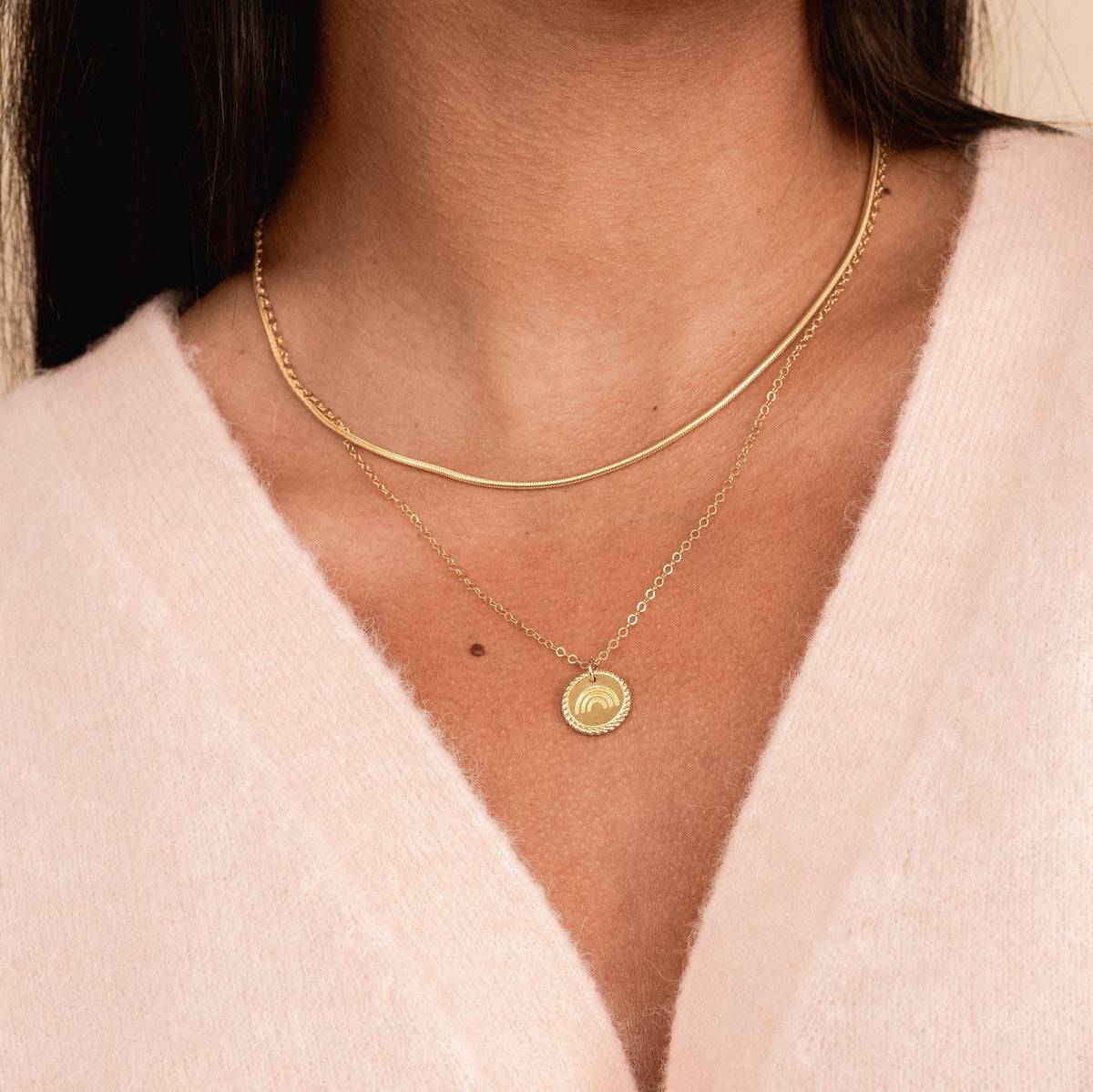 Model wearing a pink cardigan sweater while wearing a gold Snake Chain Necklace layered with the dainty gold Rainbow Necklace by Katie Dean Jewelry.